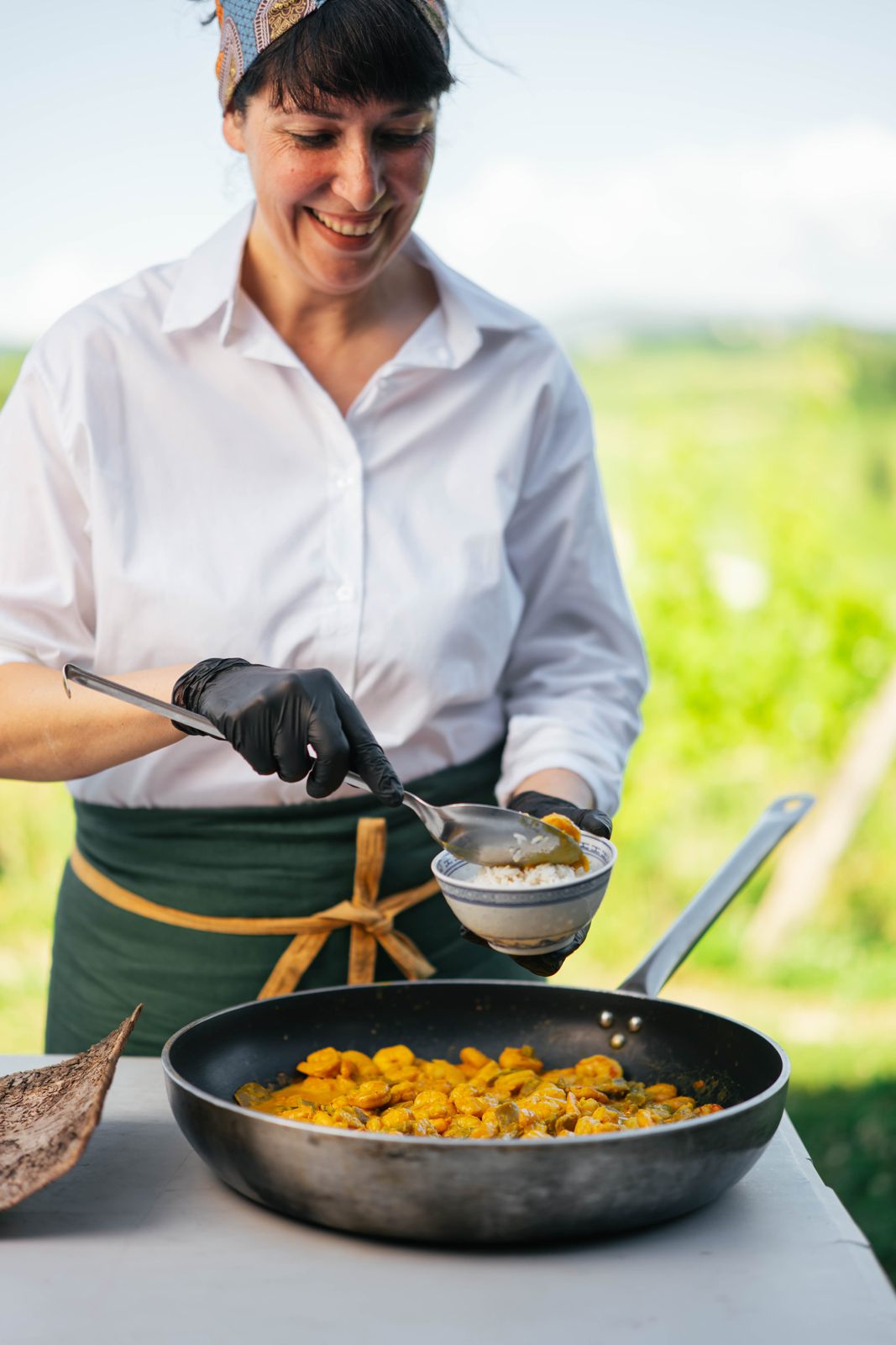 Chef Erica Parpinel smiling as she plates food from a pan outdoors